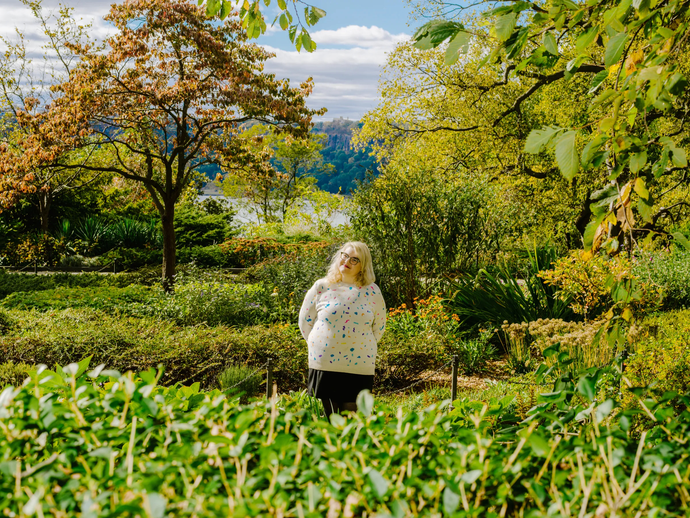 A photo of Amber Discko standing in a garden surrounded by green trees and bushes.